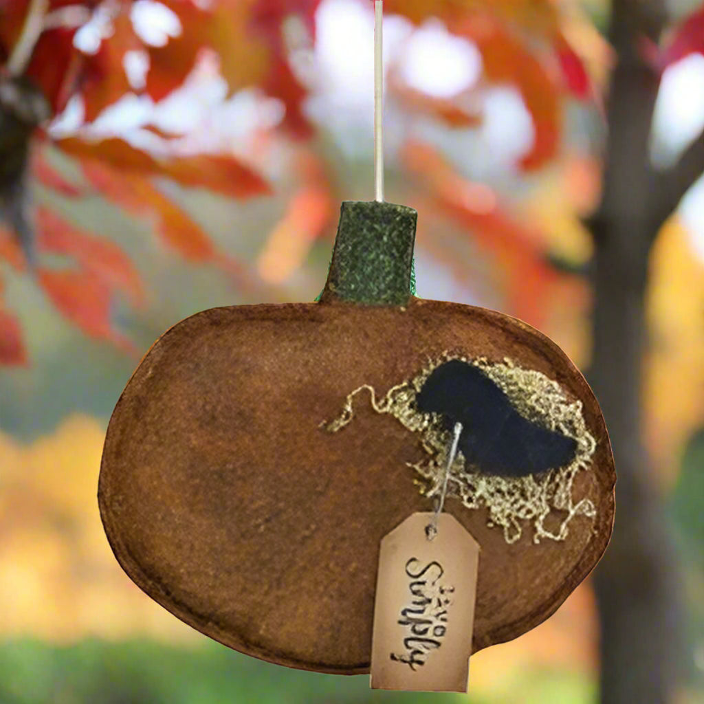 A felt pumpkin ornament with a black felt crow in a felt nest, with a green felt stem, and a tag that reads 'live simply'.
