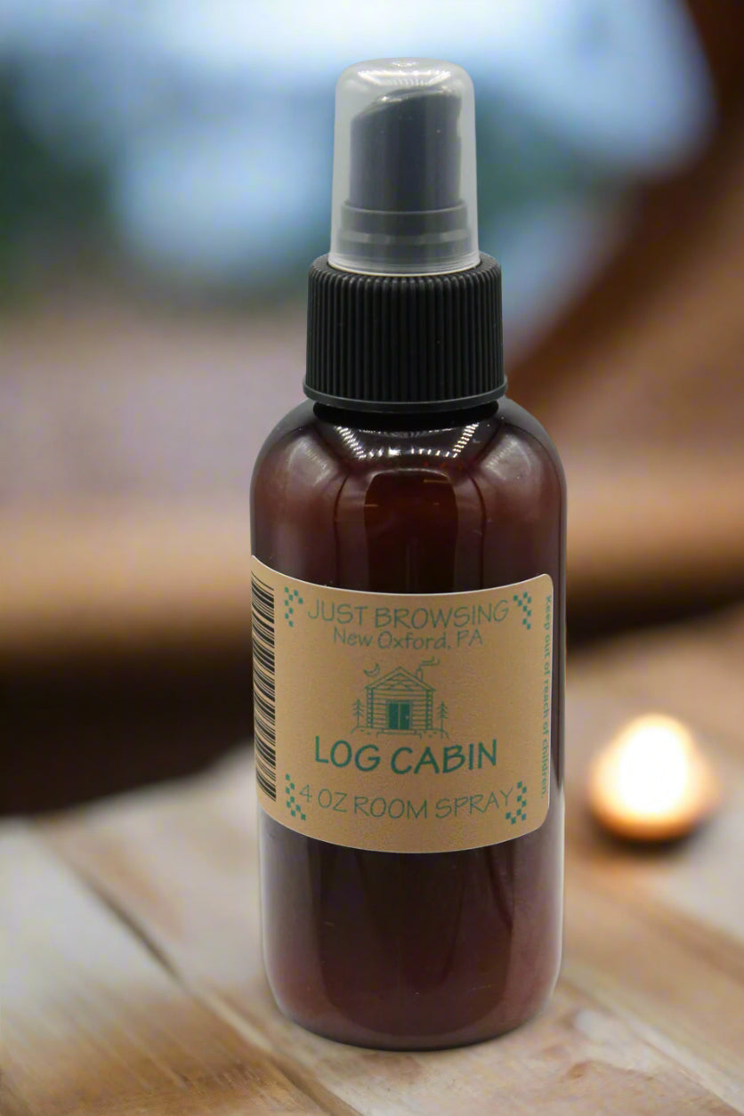Bottle of 'Log Cabin' room spray with a label on a wooden surface.