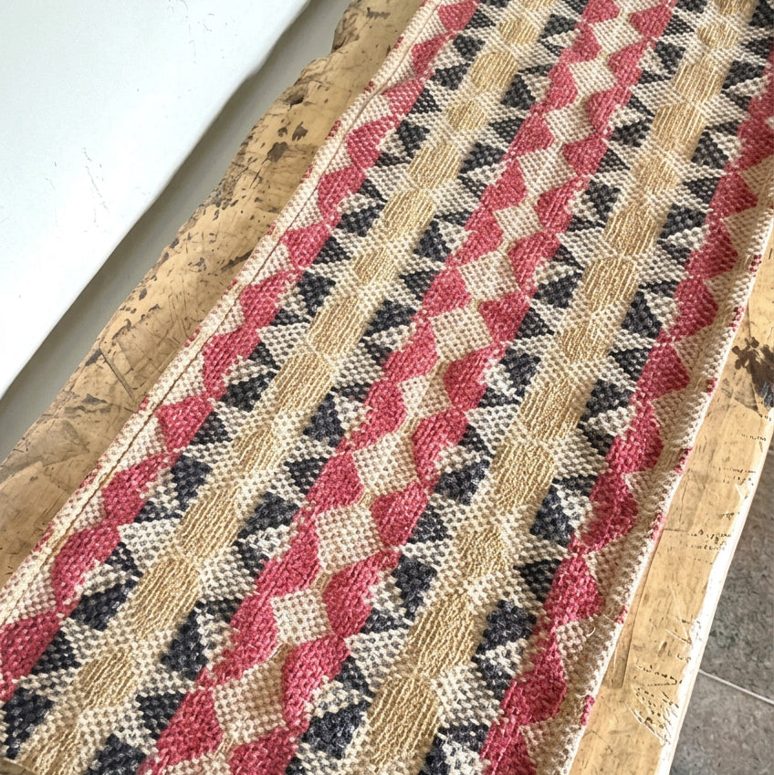 Textile with red and blue pattern on a wooden surface with a bowl of pinecones.