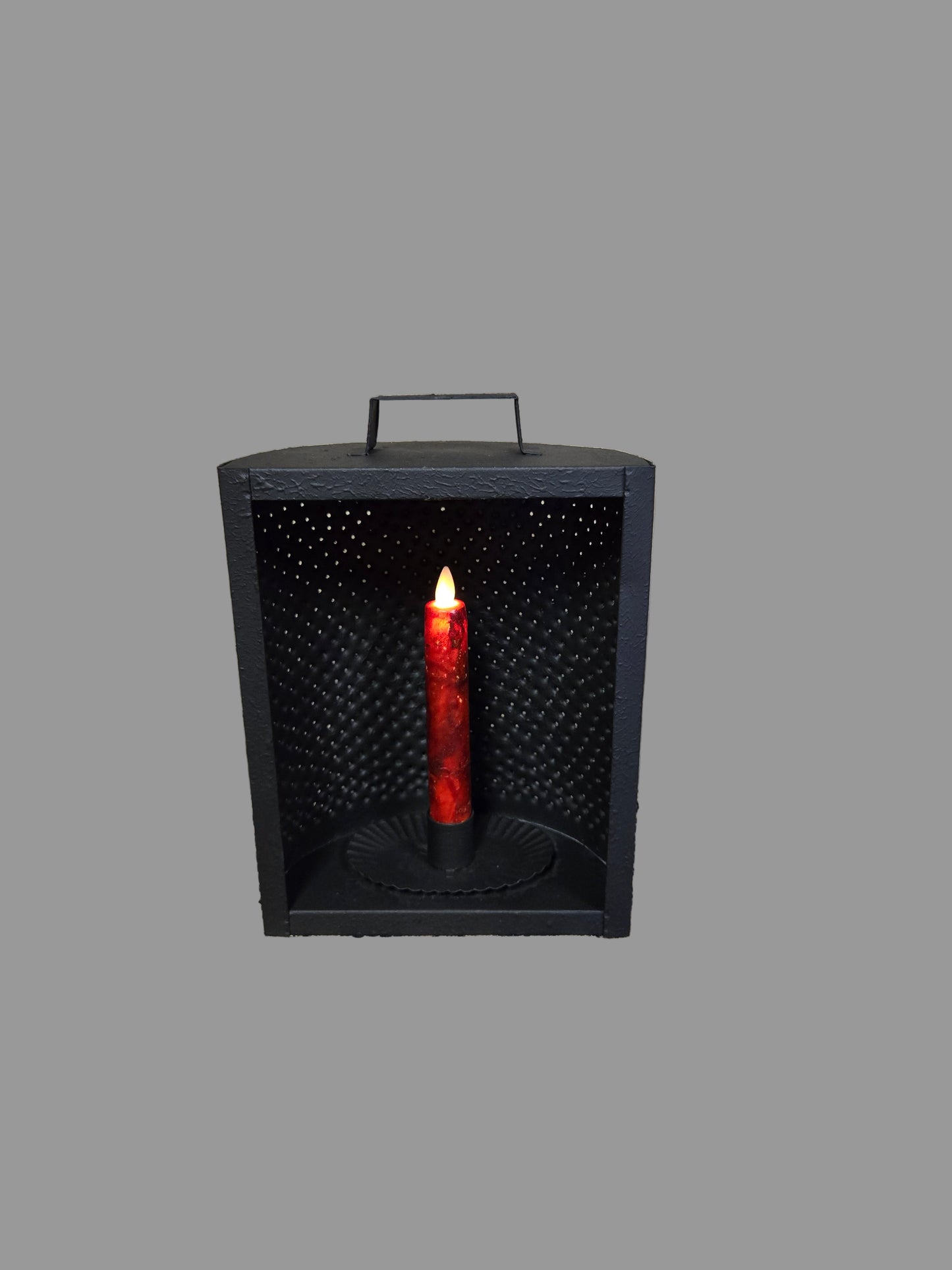 A black metal mantle light candle holder with a battery operated taper candle inside, displaying a red glow through the perforated holes.
