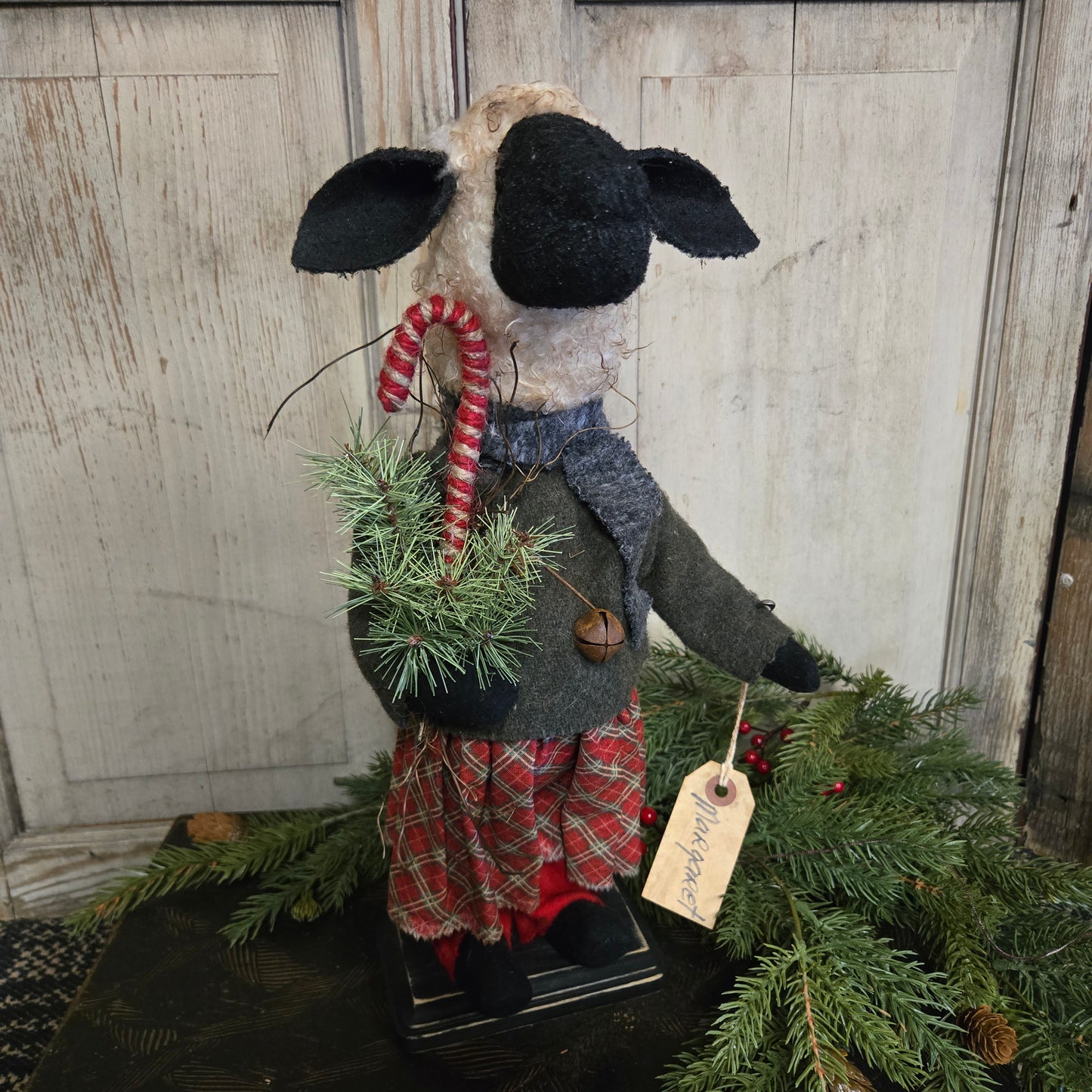Decorative sheep with a plaid outfit and candy cane, standing next to a Christmas tree on a wooden surface.