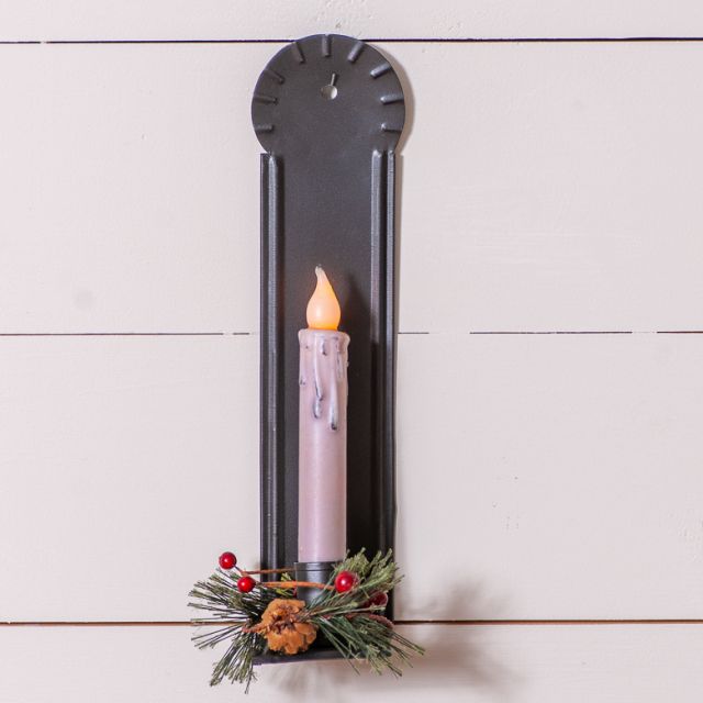 Decorative wall sconce with a lit candle and floral arrangement on a white wooden background