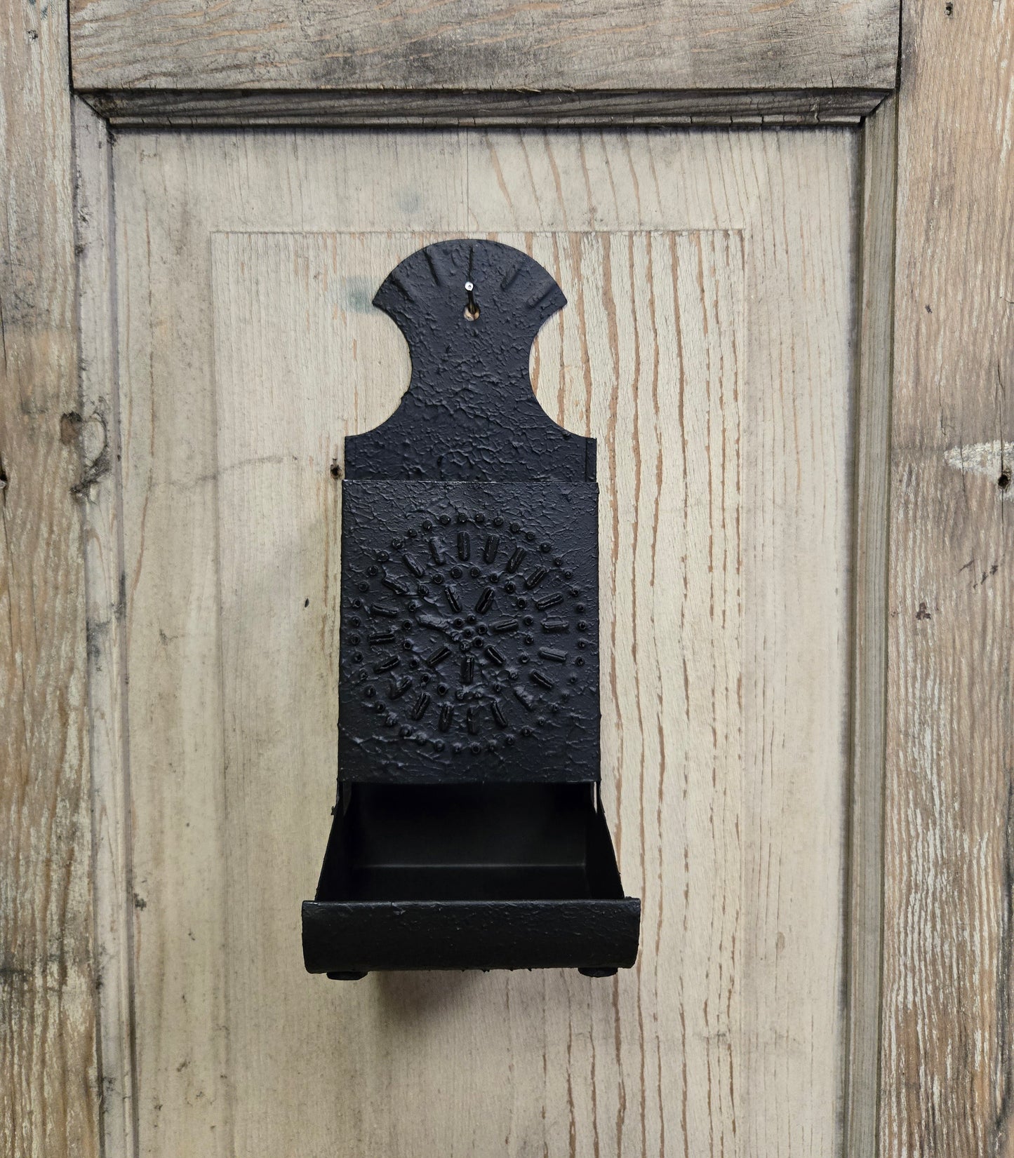 A textured black metal match box holder mounted on a wooden wall.