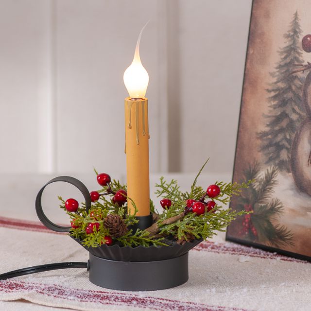 Decorative candle with greenery and berries on a table, with a painting in the background.