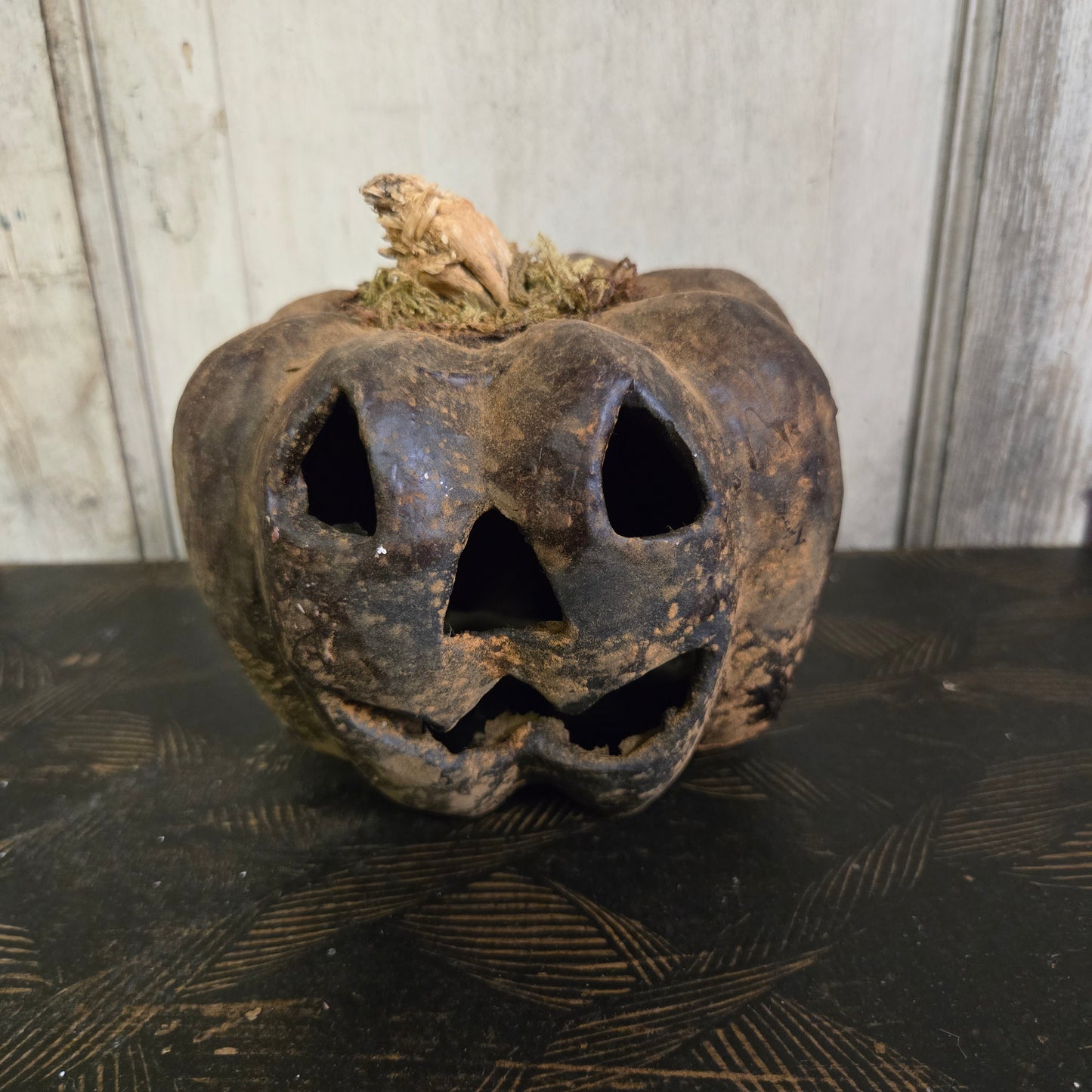 Rustic wooden pumpkin with a carved face against a textured wall.