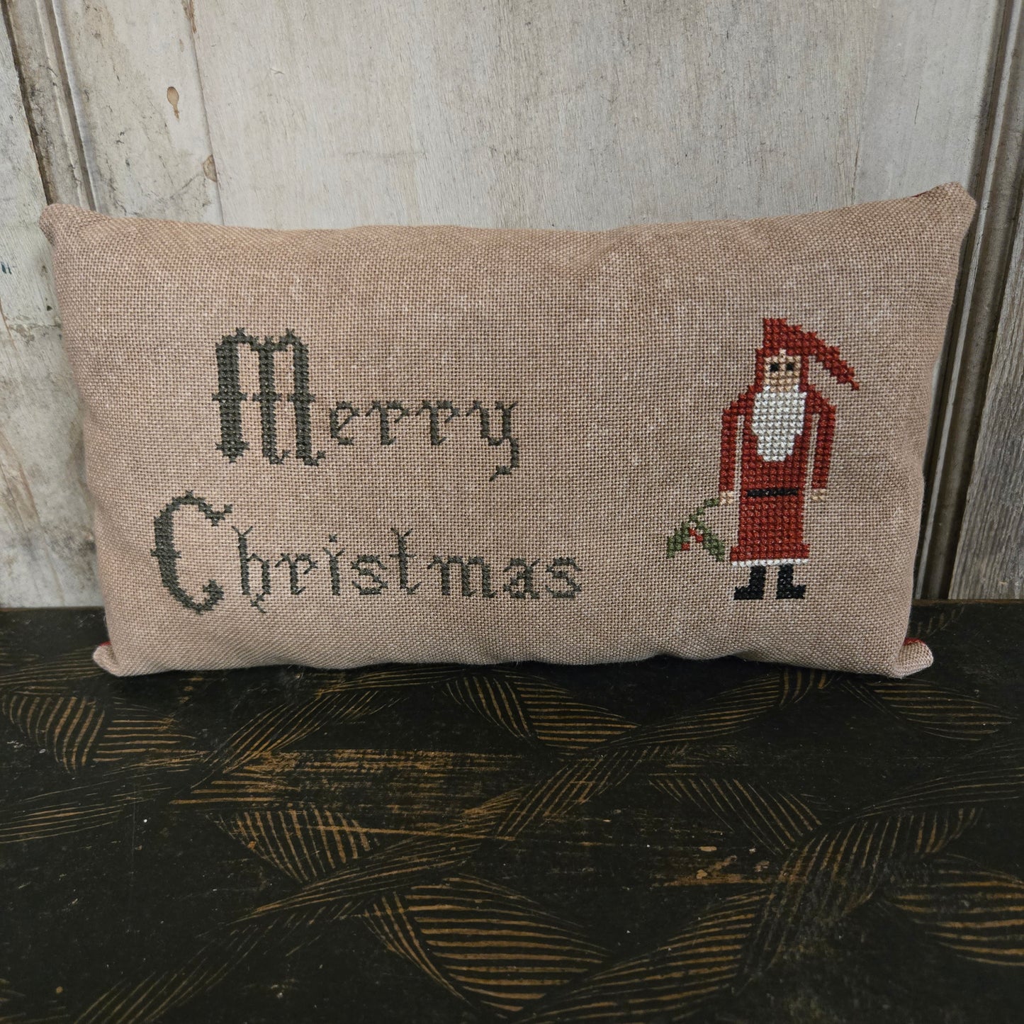 Decorative pillow with embroidered text and santa design on a wooden surface