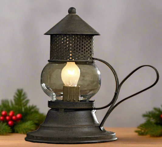 A small, vintage-style metal and glass Onion lamp with a glowing bulb, on a table surrounded by greenery