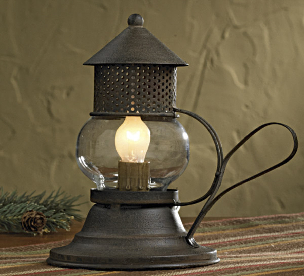 A small, vintage-style metal and glass Onion lamp with a glowing bulb, on a table surrounded by greenery