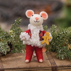 Plush toy mouse in red pants holding a gingerbread man on a wooden surface with greenery.