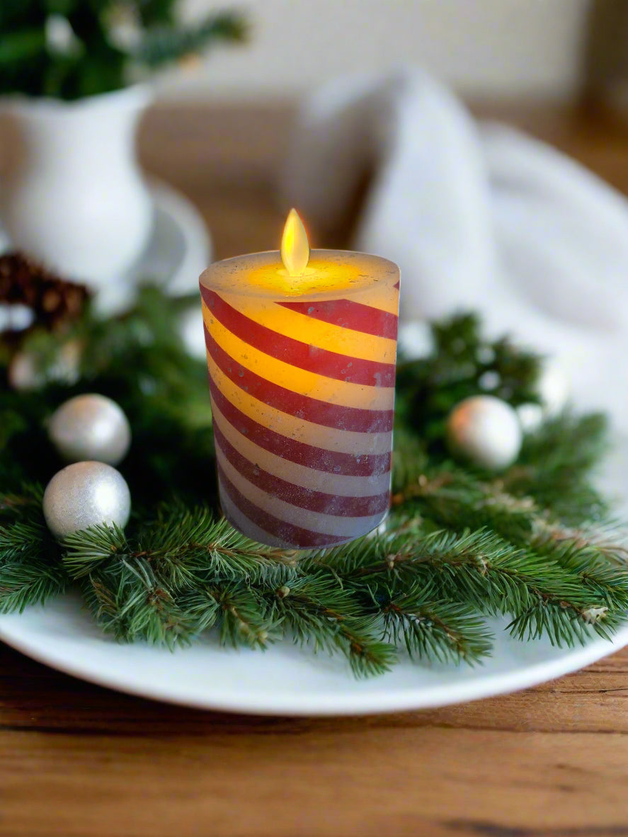 A battery-operated candle with a moving flame effect, designed to resemble a candy cane, placed on a round wooden pillar.