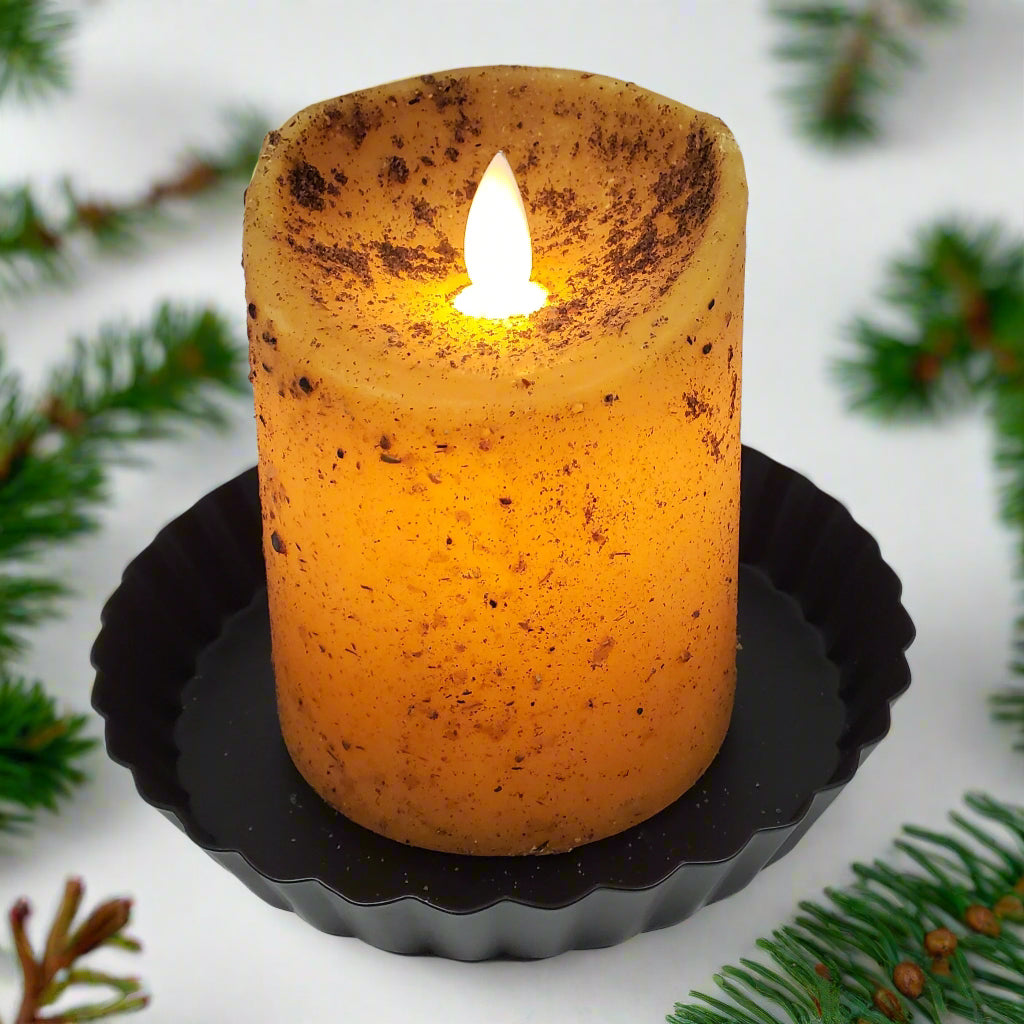 A moving flame pillar candle in a mustard yellow color, sitting on a black holder, with a visible flame at the top