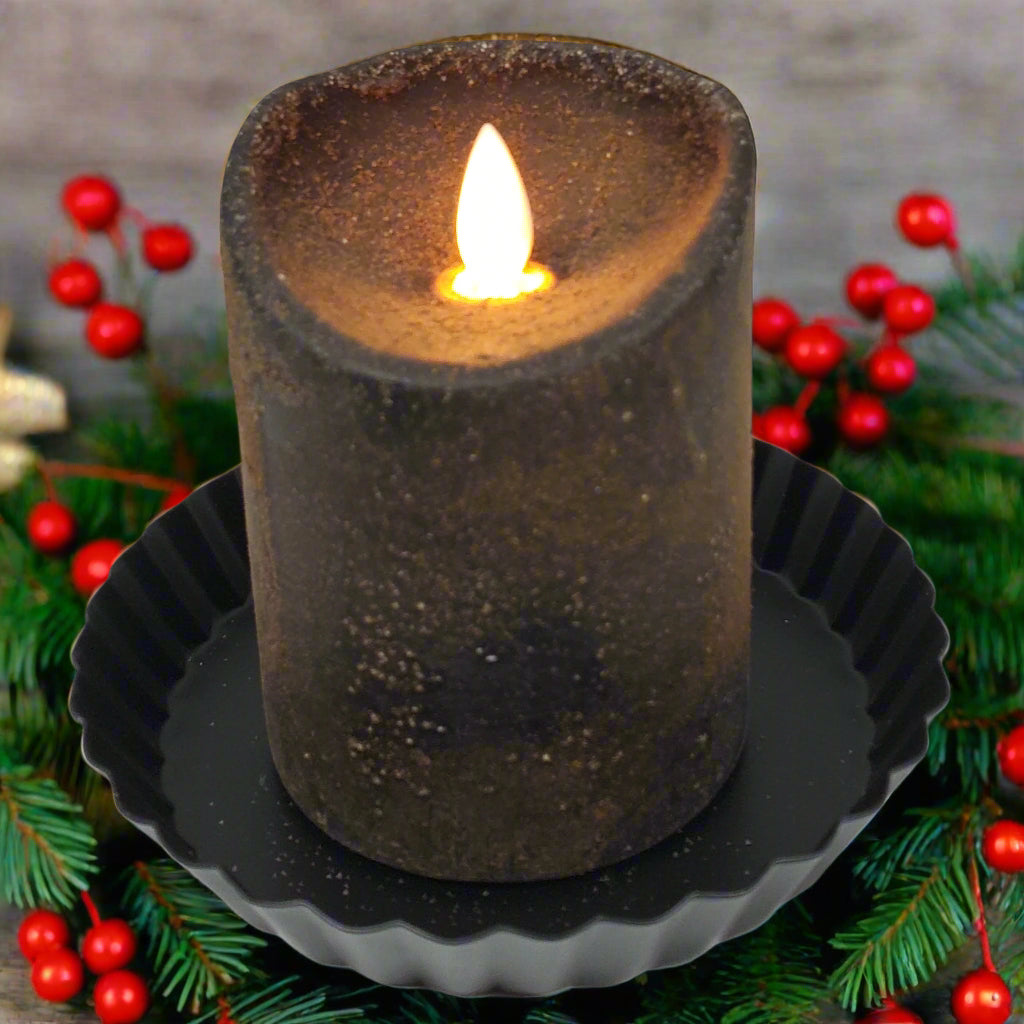 A brown pillar candle with a moving flame effect on a black holder, designed to look like it is lit from the inside.
