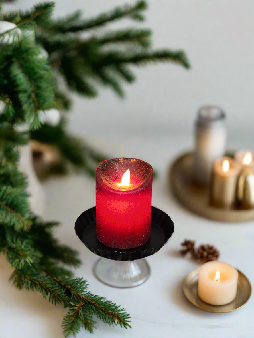 A red pillar candle with a moving flame, placed on a textured black mat, with an open door in the background.
