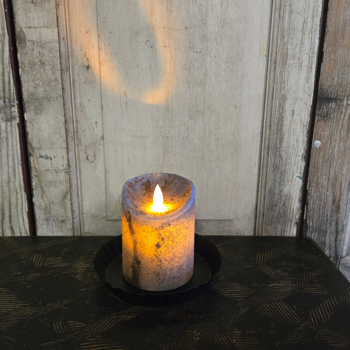 A moving flame pillar candle in robins egg blue color, placed on a black surface with a wooden background.