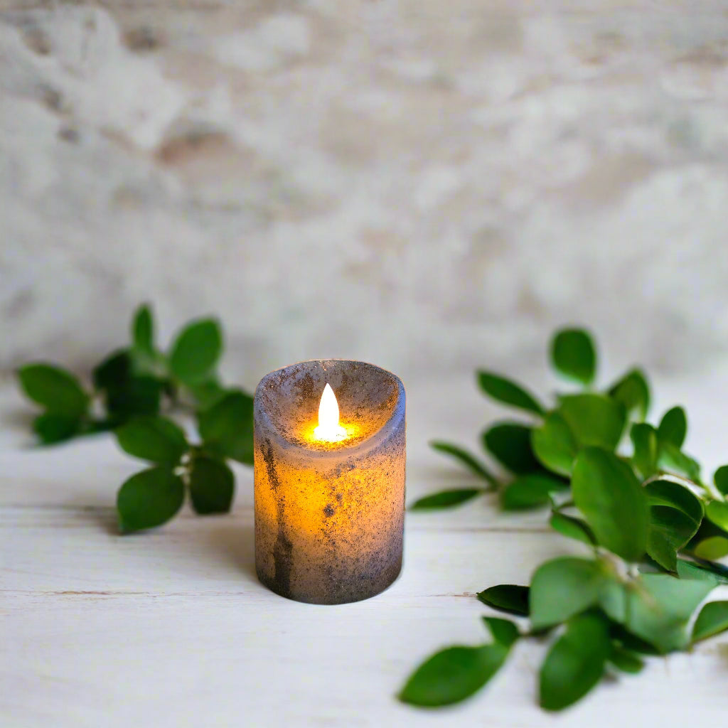 A moving flame pillar candle in robins egg blue color, placed on a black surface with a wooden background.