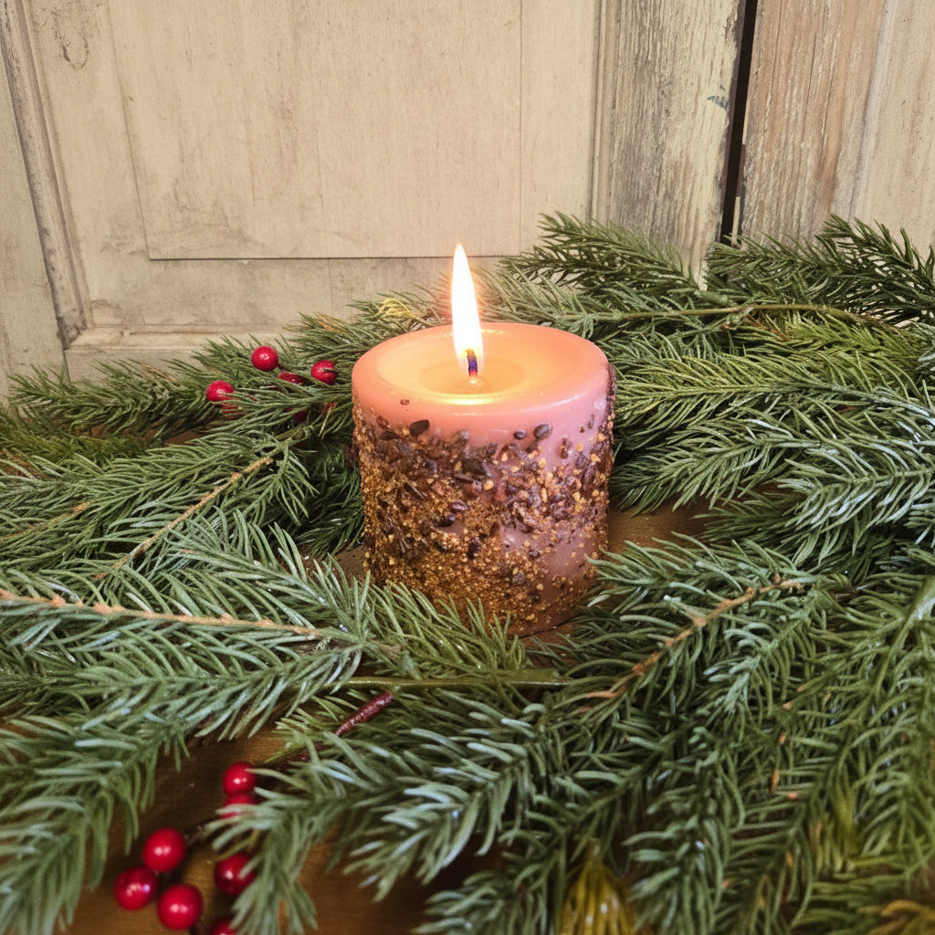 Pink candle with glitter on a bed of green pine needles and red berries against a wooden background