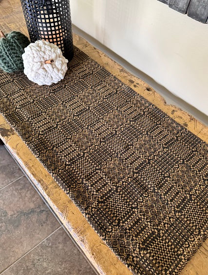 A long runner with a black and tan geometric pattern, laid out on a wooden table.
