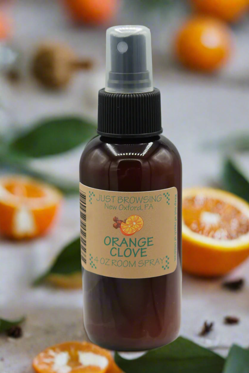 Brown glass bottle with a spray top labeled 'Orange Clove' on a gray background with oranges and cloves.