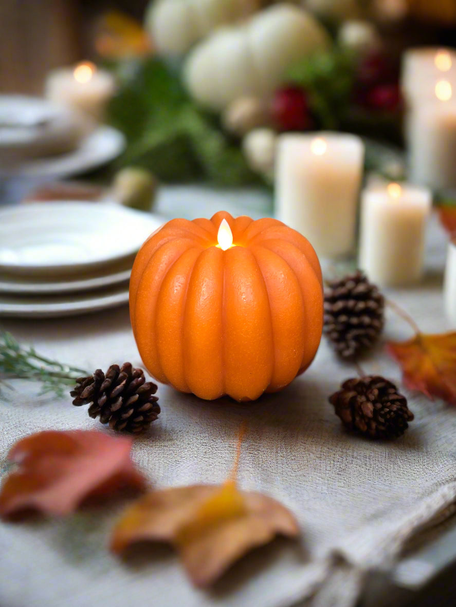 Pumpkin shaped battery operated candle on a wooden riser with greenery surrounding it