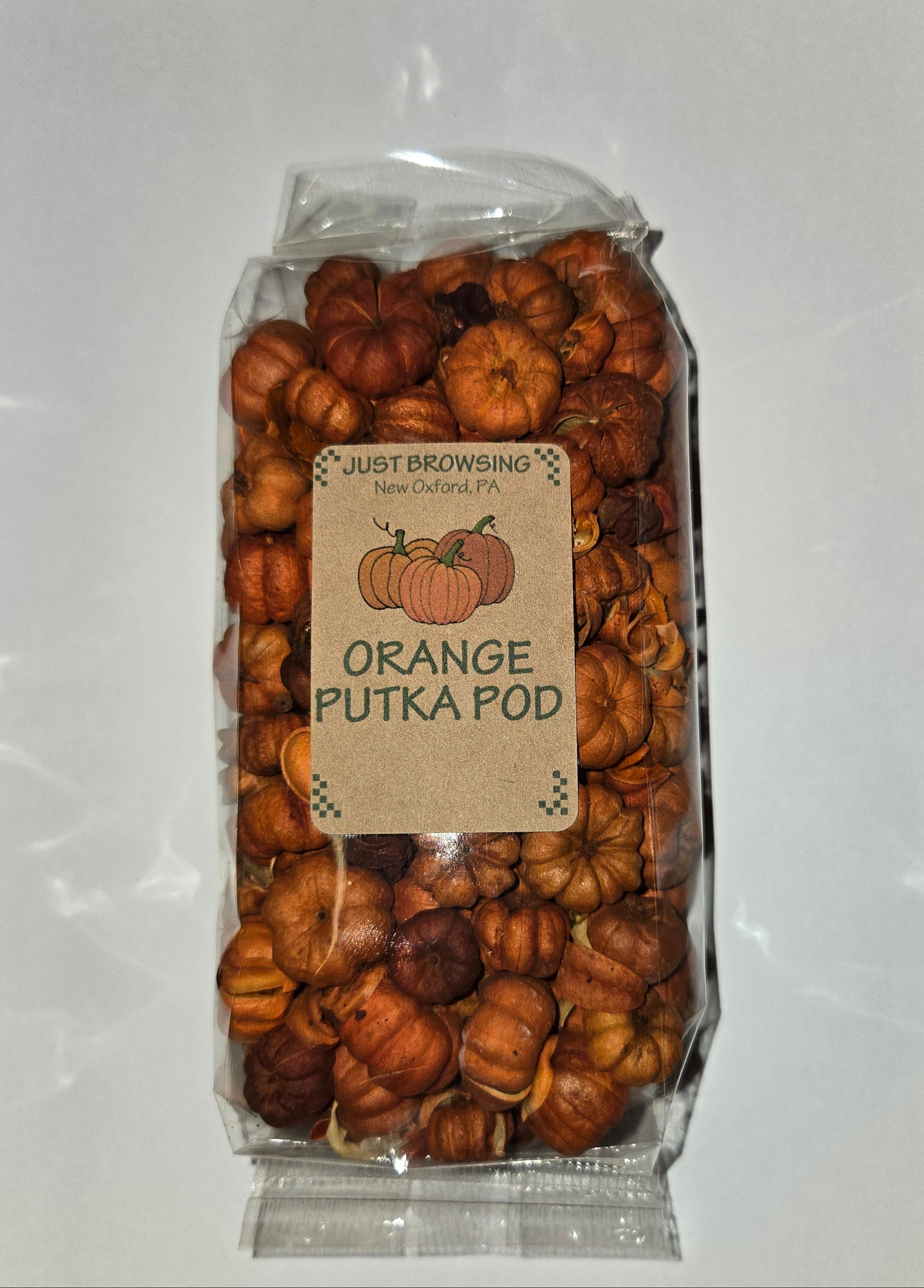 A clear plastic bag filled with dried orange-colored pod-like snacks or candies, with a kraft paper label reading 'JUST BROWSING ORANGE PUTKA POD'. The bag is photographed from above on a white sheet of paper over a speckled gray countertop.