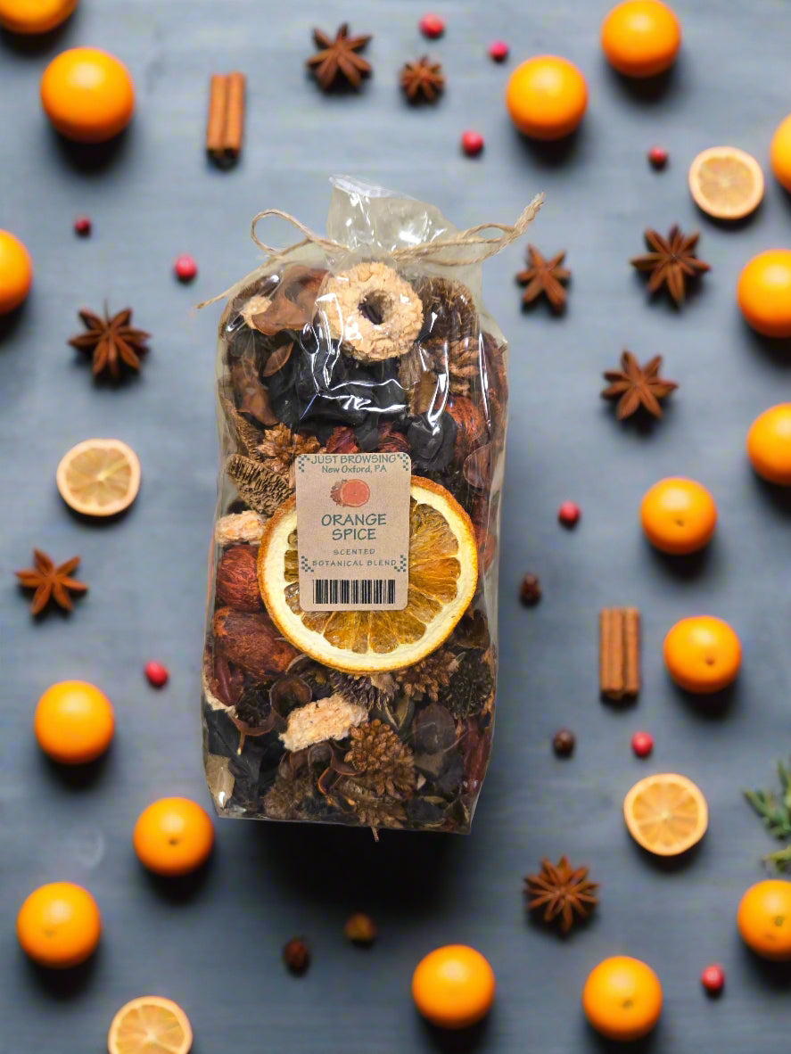 Bag of orange spice mix surrounded by oranges, cinnamon sticks, and star anise on a dark surface.