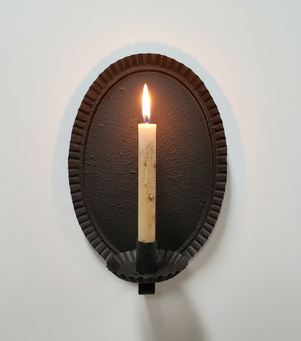 A black oval-shaped metal sconce with a textured finish, designed to hold a battery taper candle.