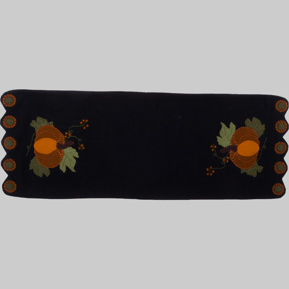 A black table runner with a whimsical pumpkin design featuring orange and yellow accents, made of wool felt.