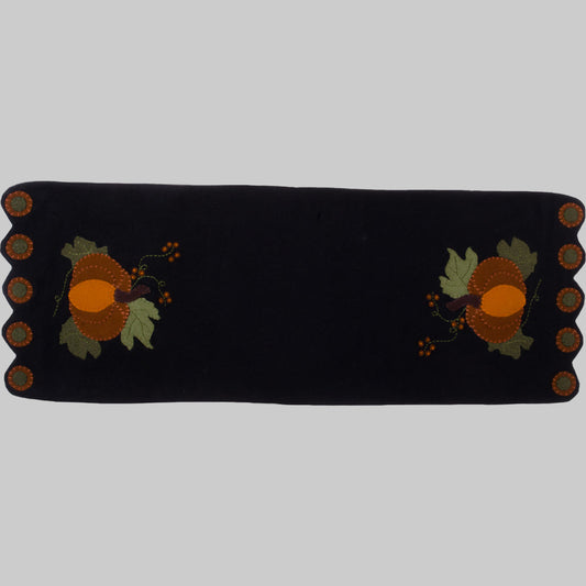 A black table runner with a whimsical pumpkin design featuring orange and yellow accents, made of wool felt.