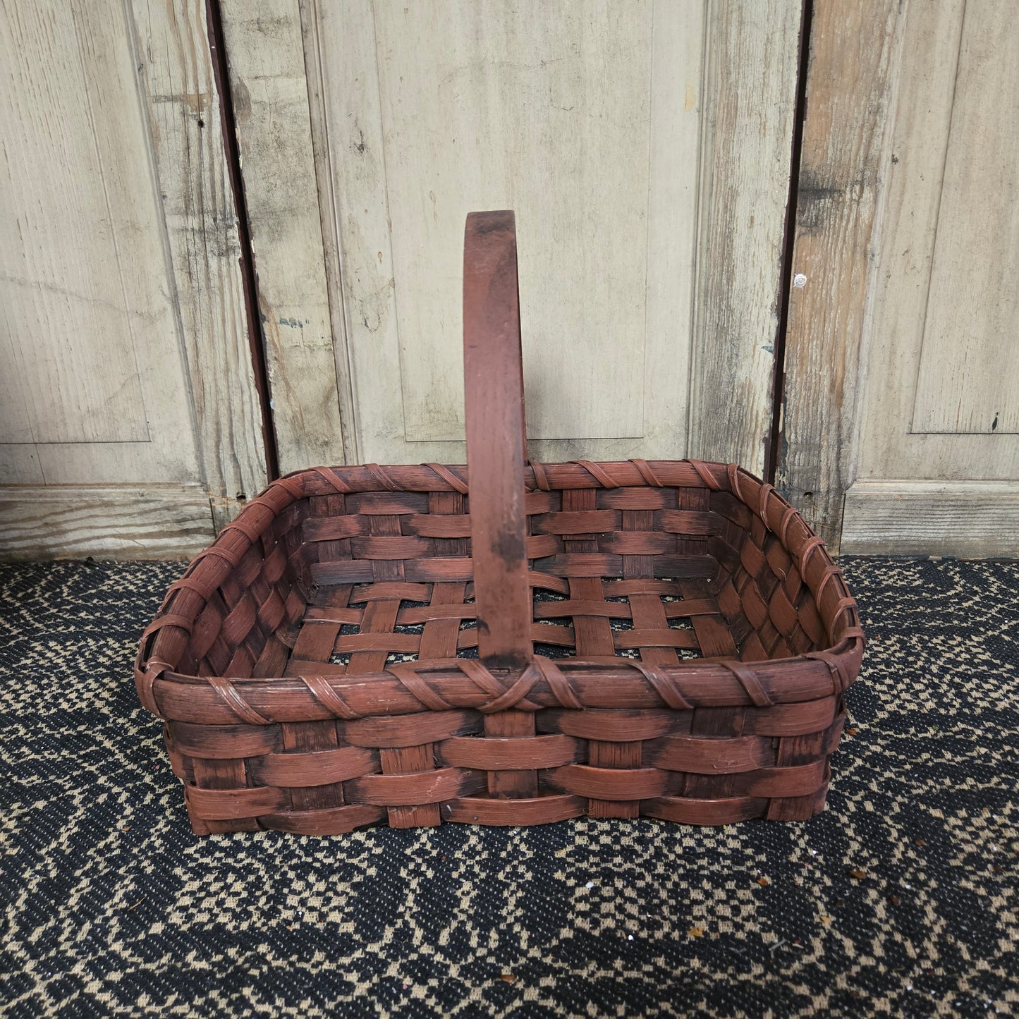 Burgundy hand woven basket sitting in front of a weathered wood door
