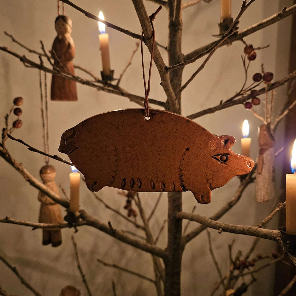 Pig-shaped redware ornament with a warm brown glaze, etched details, and a rustic hanging cord.