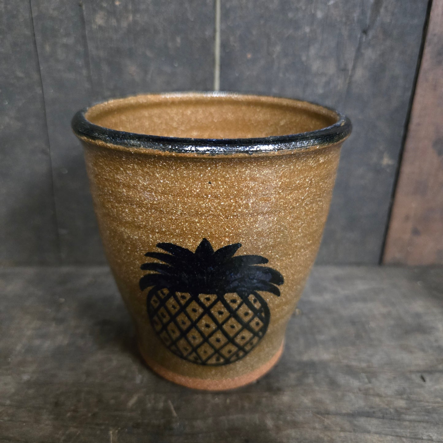 Brown ceramic cup with black pineapple design on a dark stone surface