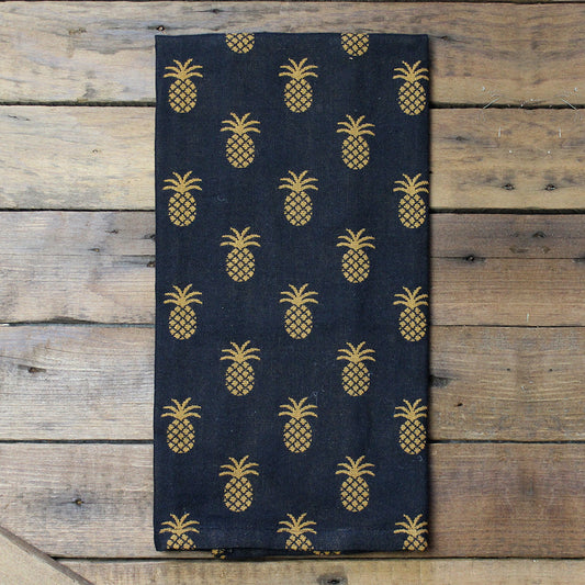 A black hand towel with a pineapple pattern laid out on a wooden surface.