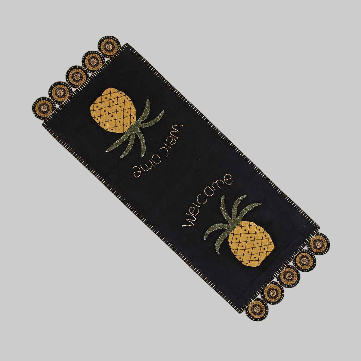 A black table runner with a pineapple motif and the word 'welcome' embroidered in yellow and green.