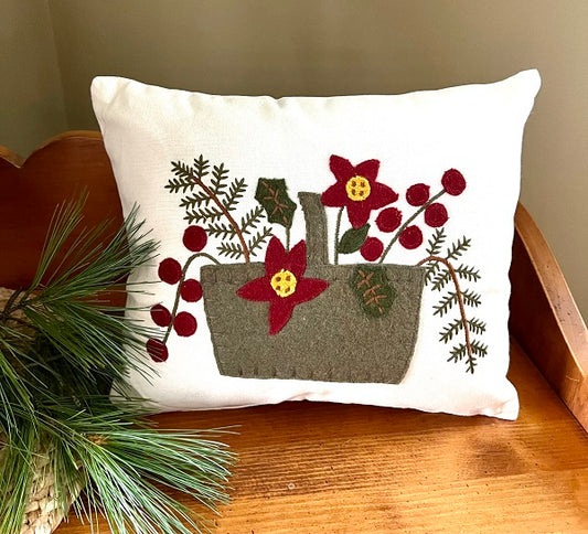 A throw pillow with a poinsettia design featuring red berries on a white background, placed on a wooden surface.