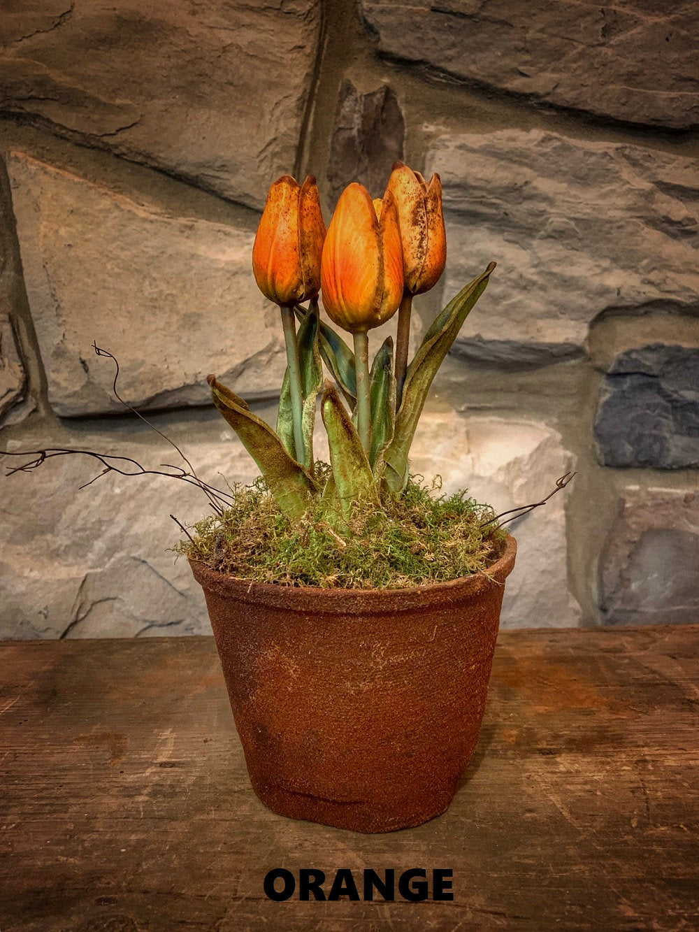 A wax dipped orange tulip decoration placed on a surface with a stone wall background.