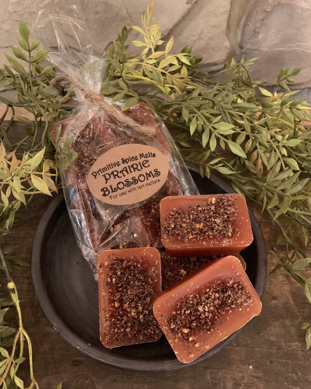 A package of wax melts next to unwrapped wax pieces in a bowl surrounded by greenery