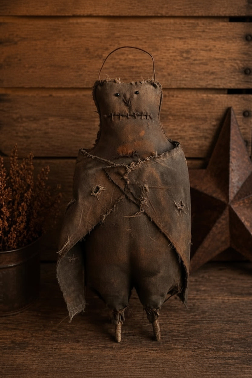 A handmade Primitive Kreation 'Primitive Bat' doll made from dark brown leather and fabric, featuring a stitched face, tattered cape, and a hanging tag, set against a rustic wooden background with a star decoration.