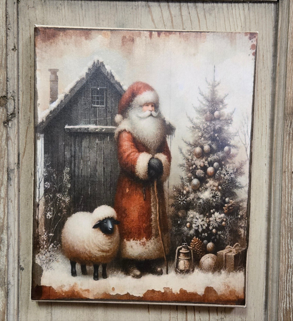 A canvas print depicting a traditional image of Santa Claus standing next to a sheep with a lantern, in a snowy setting with a Christmas tree and a cabin in the background.