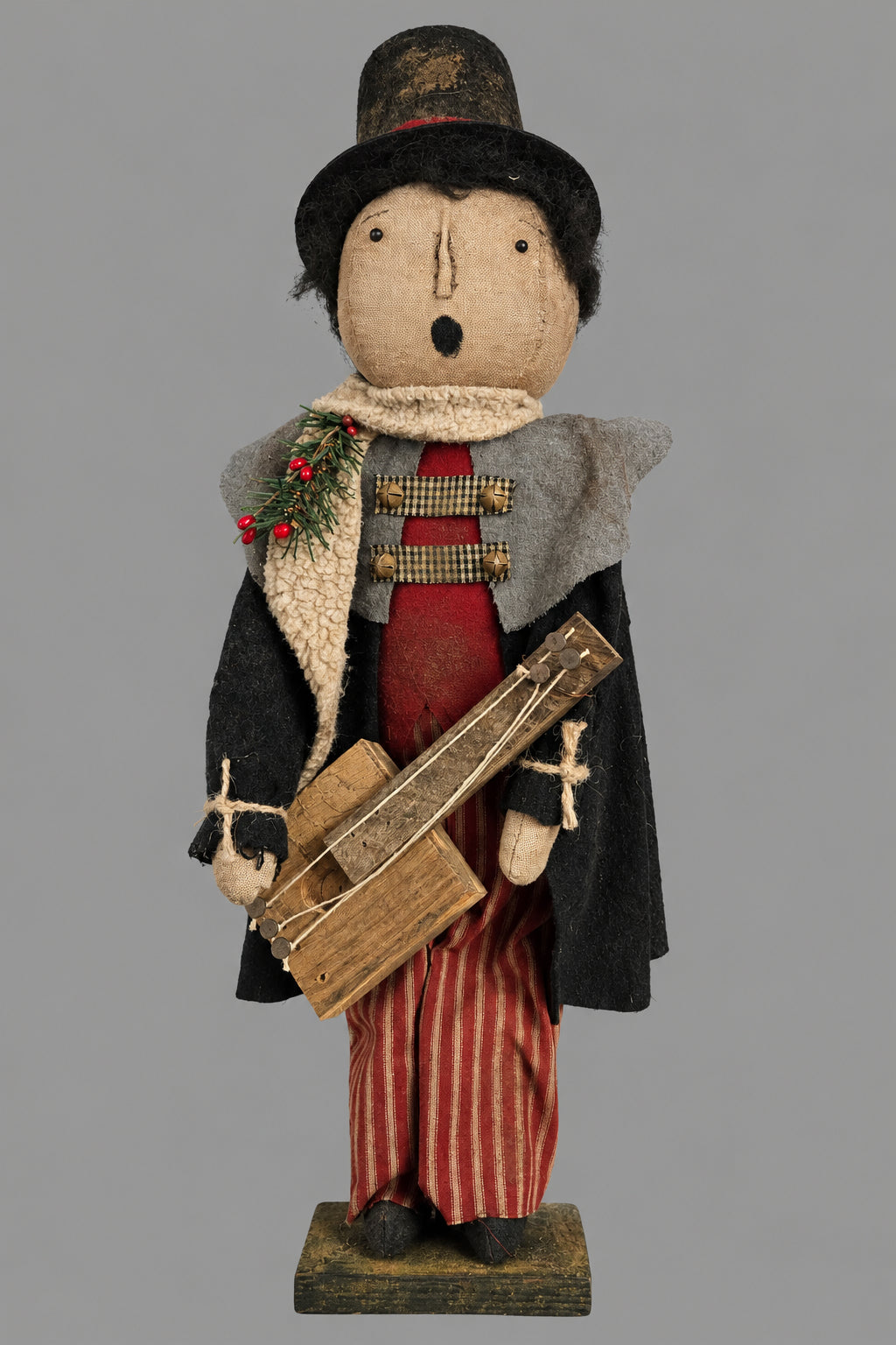 Doll figure of a caroler with a guitar standing on a wood base against a grey background.