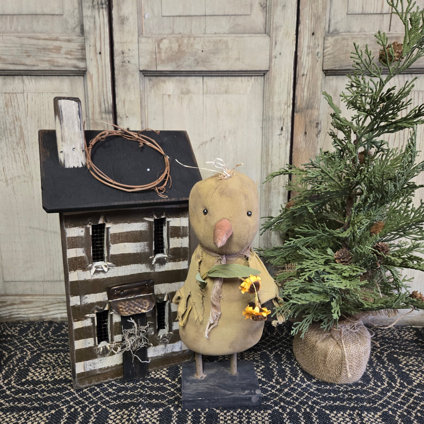A rustic yellow chick decoration with a striped hat and a flower decoration, standing next to a greenery decoration.