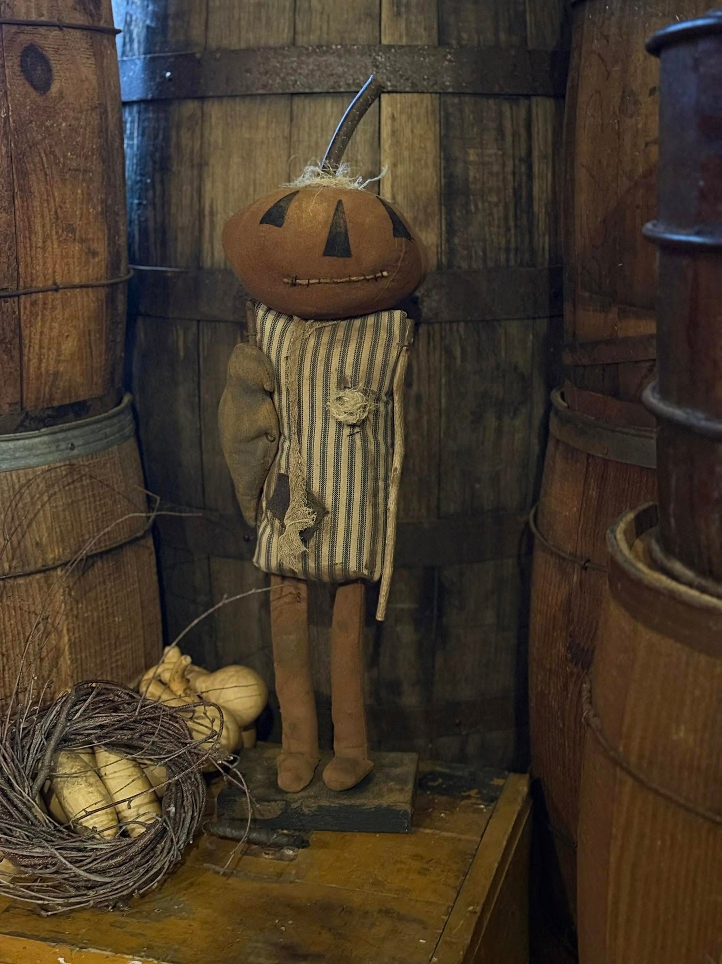 Pumpkin-headed figure in a rustic setting with wooden barrels and pumpkins.