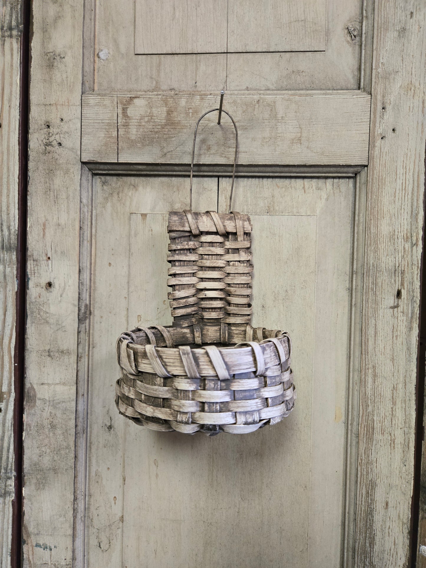 A handmade primitive cupboard basket with a buttermilk color, hanging against a rustic wooden background.