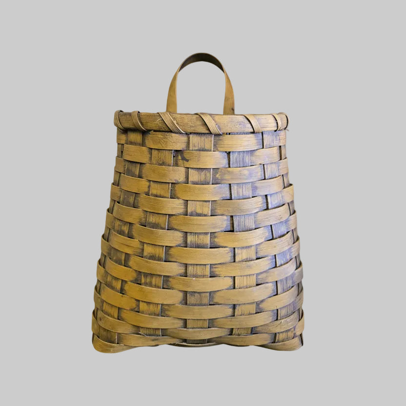 A primitive deep door basket in mustard color, hanging against a wooden background.