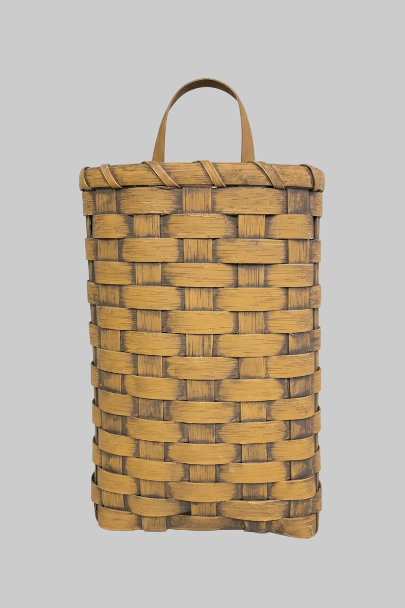 A woven basket hanging on a wooden door, primarily beige in color with brown stripes, likely handcrafted.