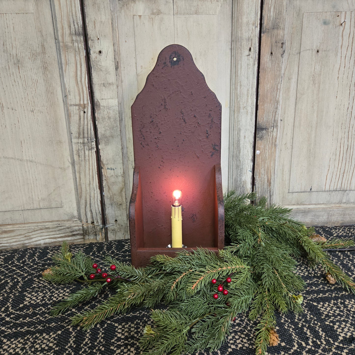 A burgundy-colored wooden electric candle holder with a lit candle inside, placed on a table with a decorative item to the side.