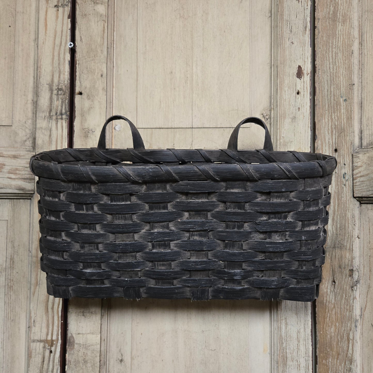 A black woven basket with handles, displayed against a wooden background.
