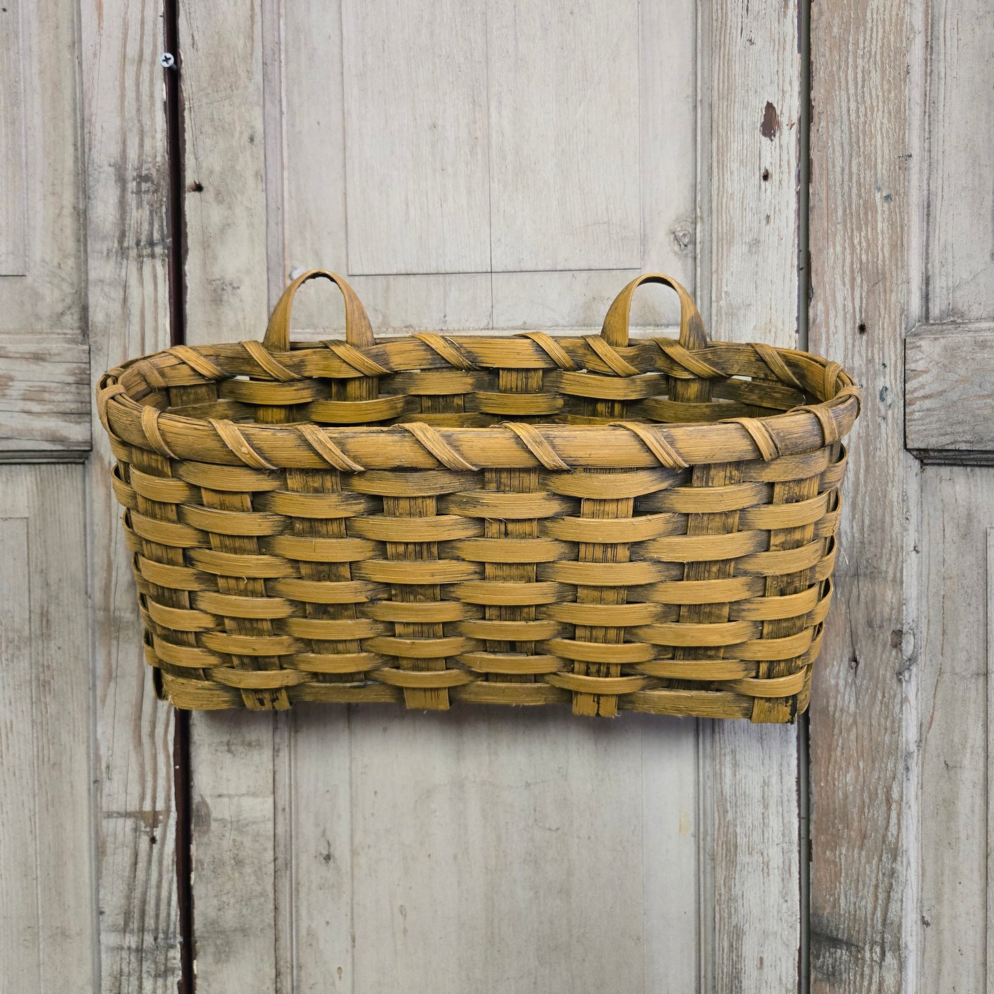A woven basket with a mustard yellow color, hanging on a wooden wall, suitable for organizing envelopes or small items.
