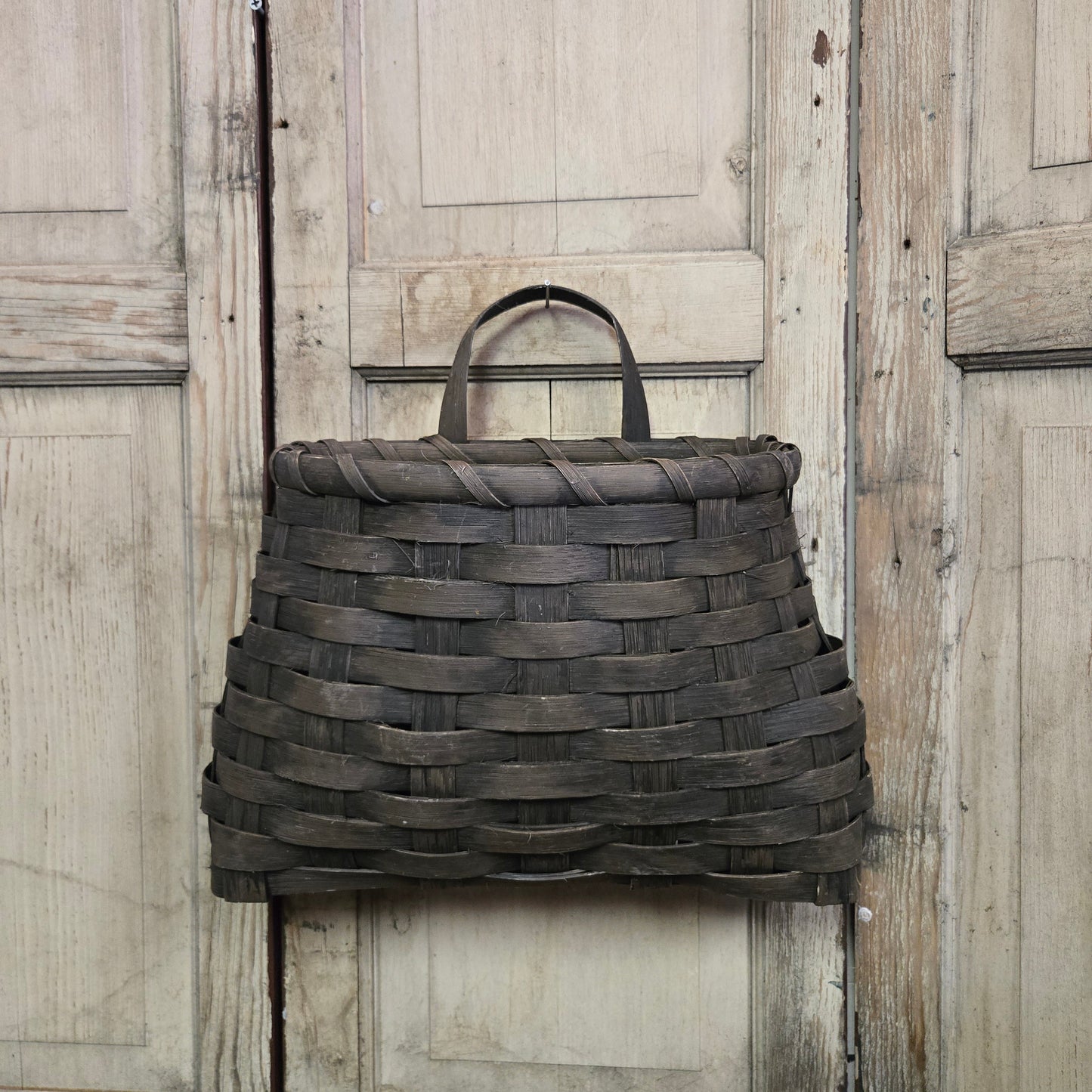 A large black woven wall basket hanging on a wooden door.
