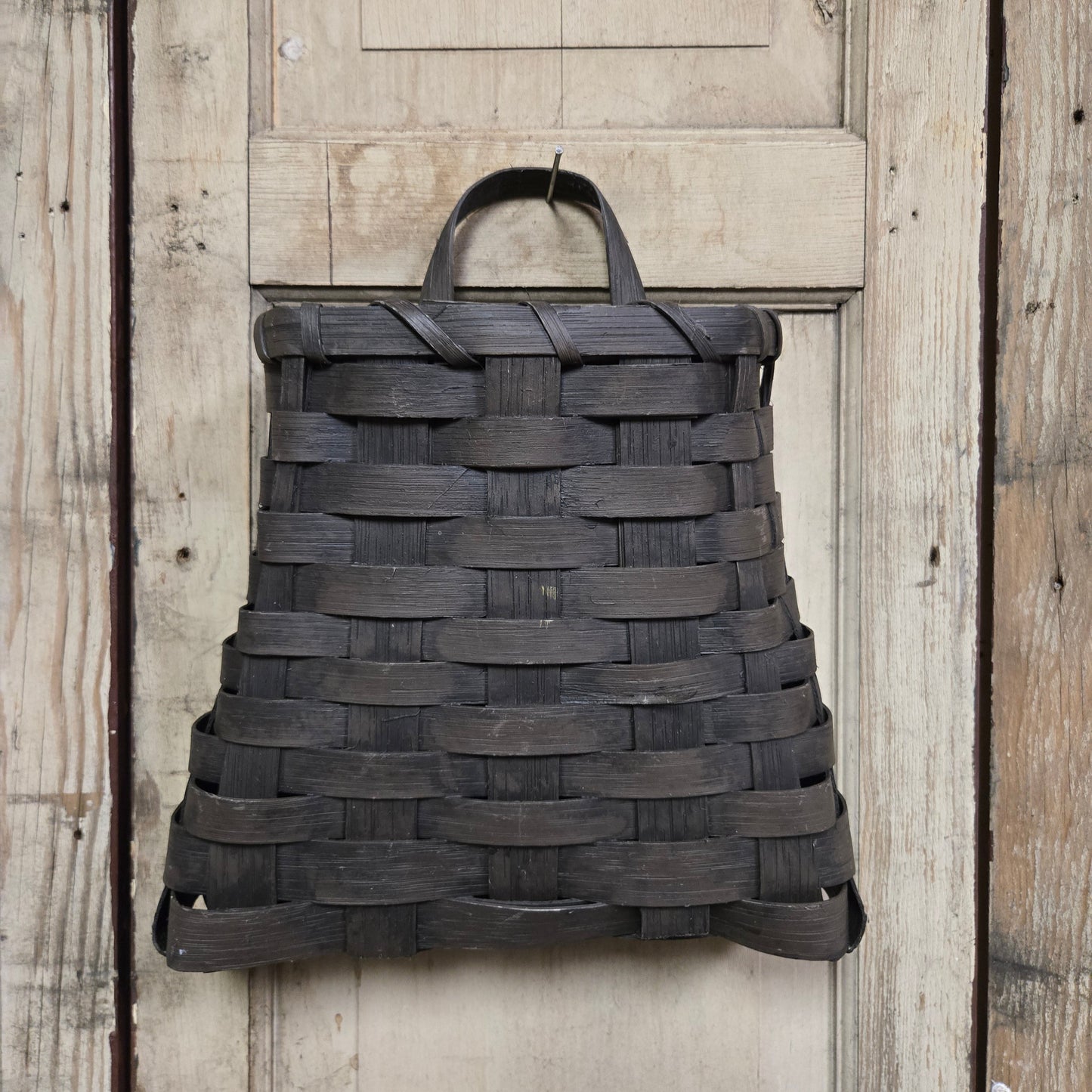 A small black woven wall basket hanging against a wooden background.