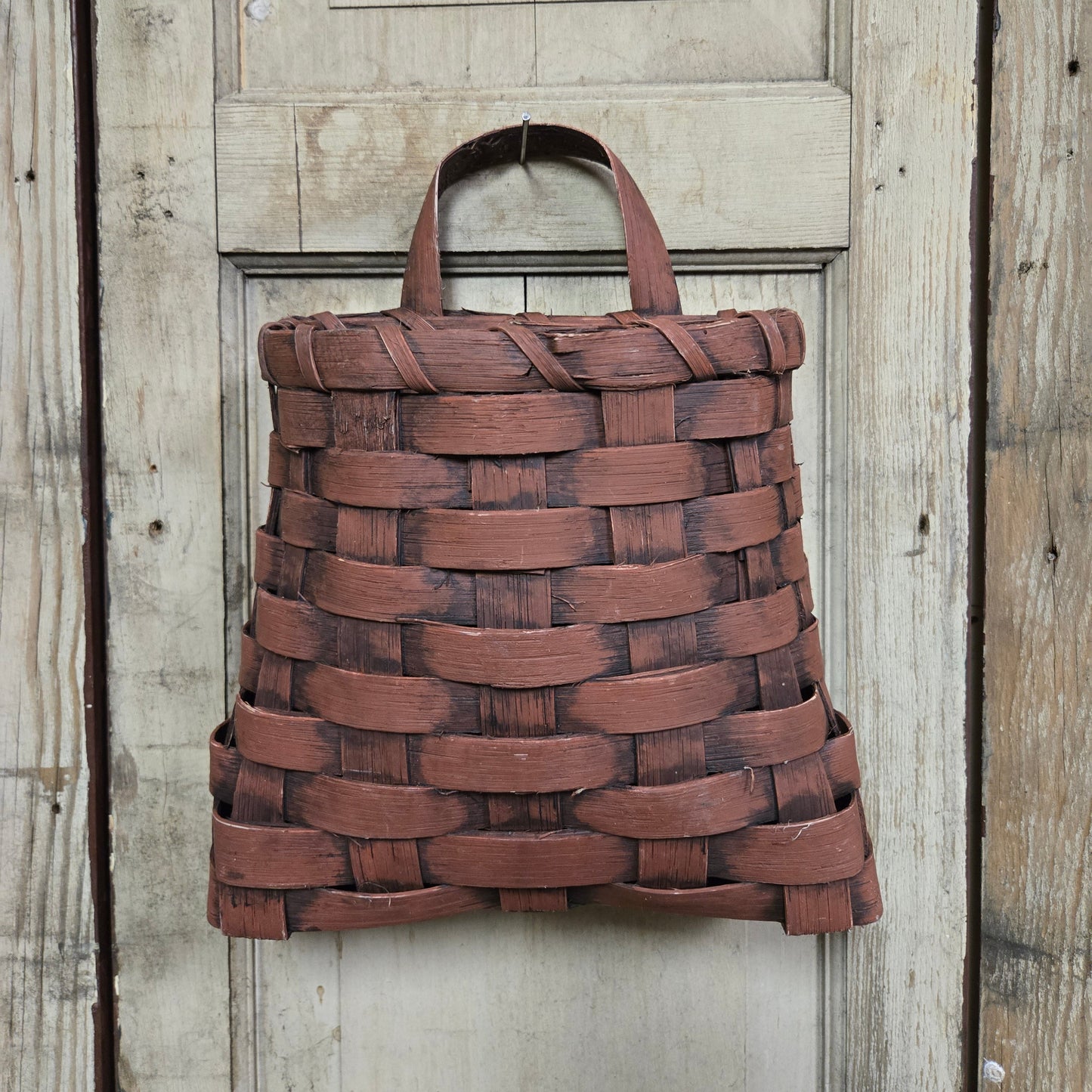A small burgundy woven wall basket hanging against a wooden background.